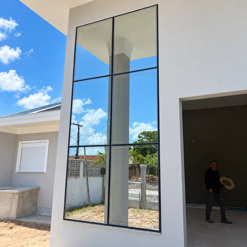 Janela alta de esquadria preta com vidro na fachada de uma casa em obra